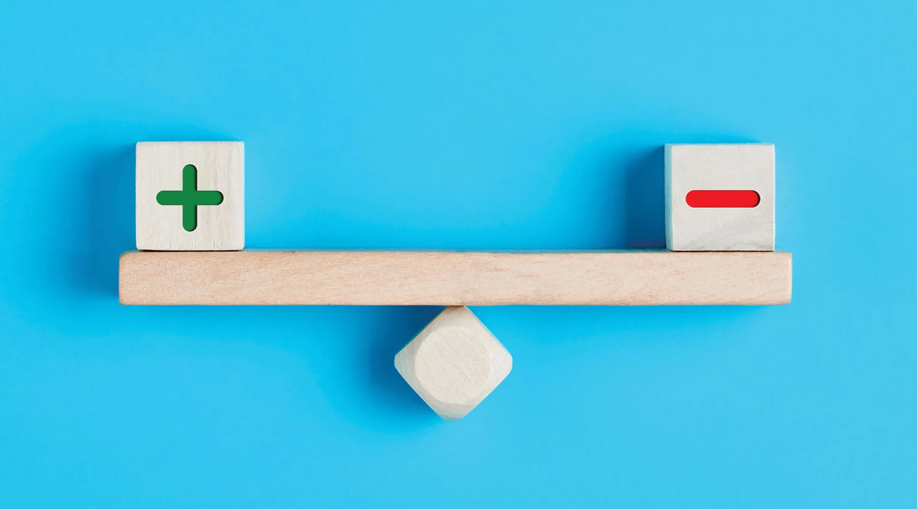 Wooden balance with positive sign and negative sign blocks.