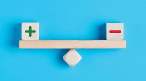 Wooden balance with positive sign and negative sign blocks.