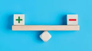 Wooden balance with positive sign and negative sign blocks.