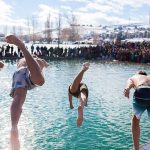 People diving into a pool with an audience watching in excitement.