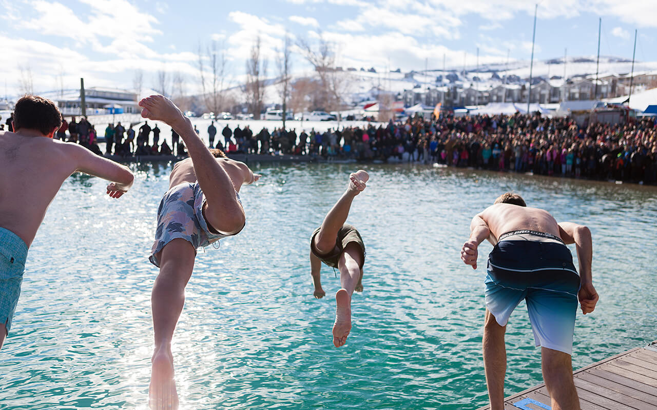 People diving into a pool with an audience watching in excitement.