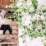 A woman sitting on a wooden staircase with a laptop, working diligently on her tasks.