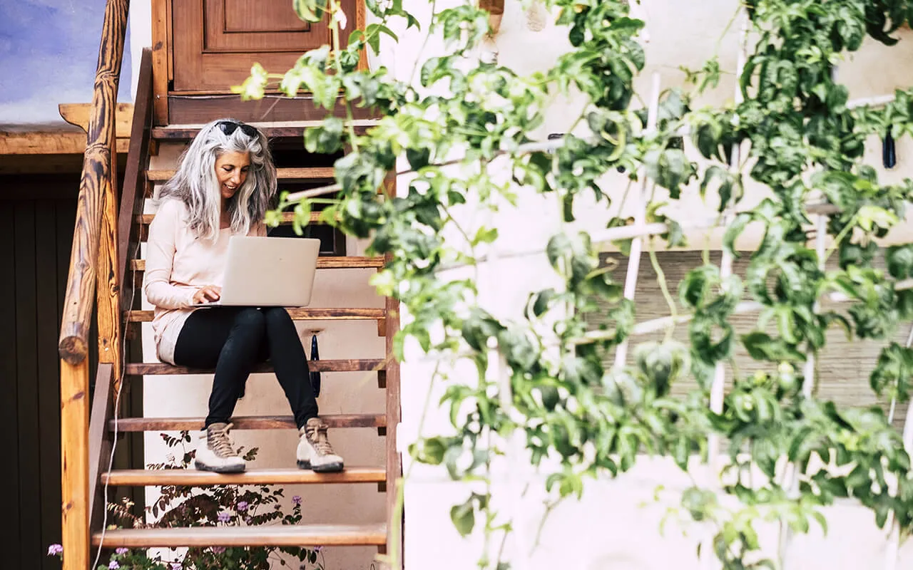 A woman sitting on a wooden staircase with a laptop, working diligently on her tasks.