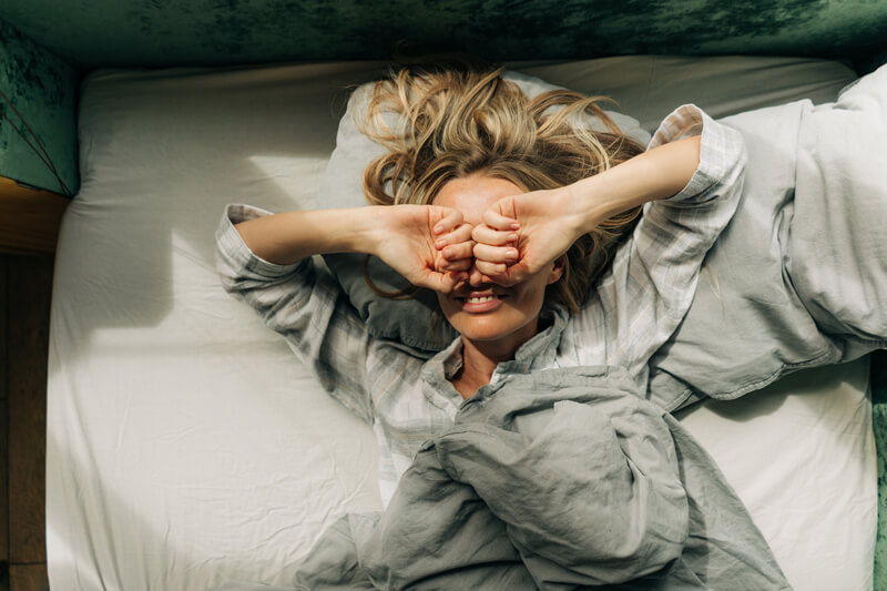 A woman lying in bed, looking slightly disheveled, as if she has just woken up from sleep.