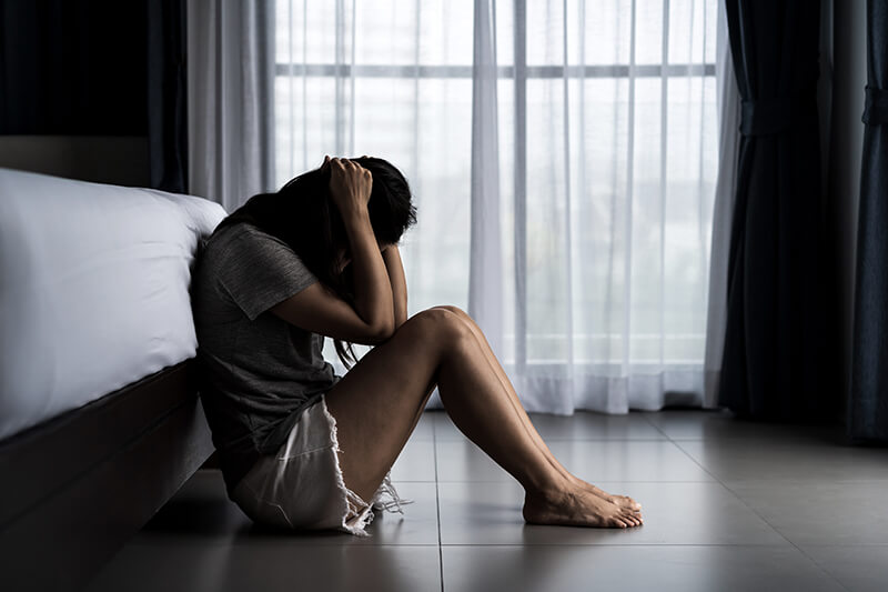 A woman sitting on the floor in front of a bed.