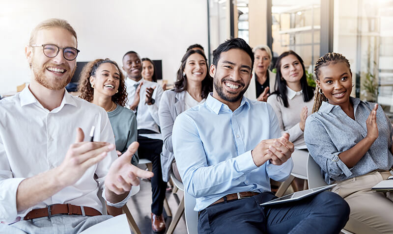 A diverse group of students in a classroom clapping enthusiastically.