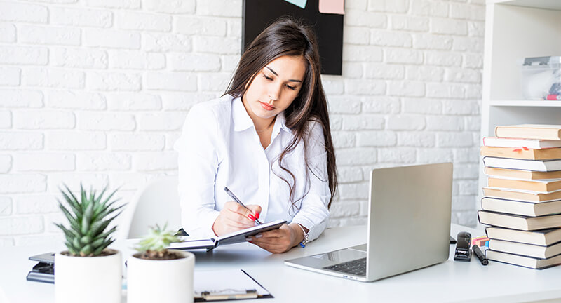 A woman sitting at a desk with a laptop and a notebook.