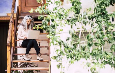 A woman sitting on a wooden staircase with a laptop, working diligently on her tasks.