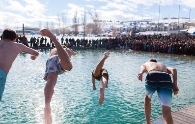 People diving into a pool with an audience watching in excitement.